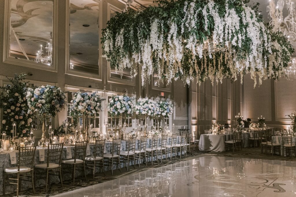 Interior photo of a wedding at the Adolphus Hotel in Dallas with stunning flower centerpieces and hanging florals from the light fixtures in dim lighting.