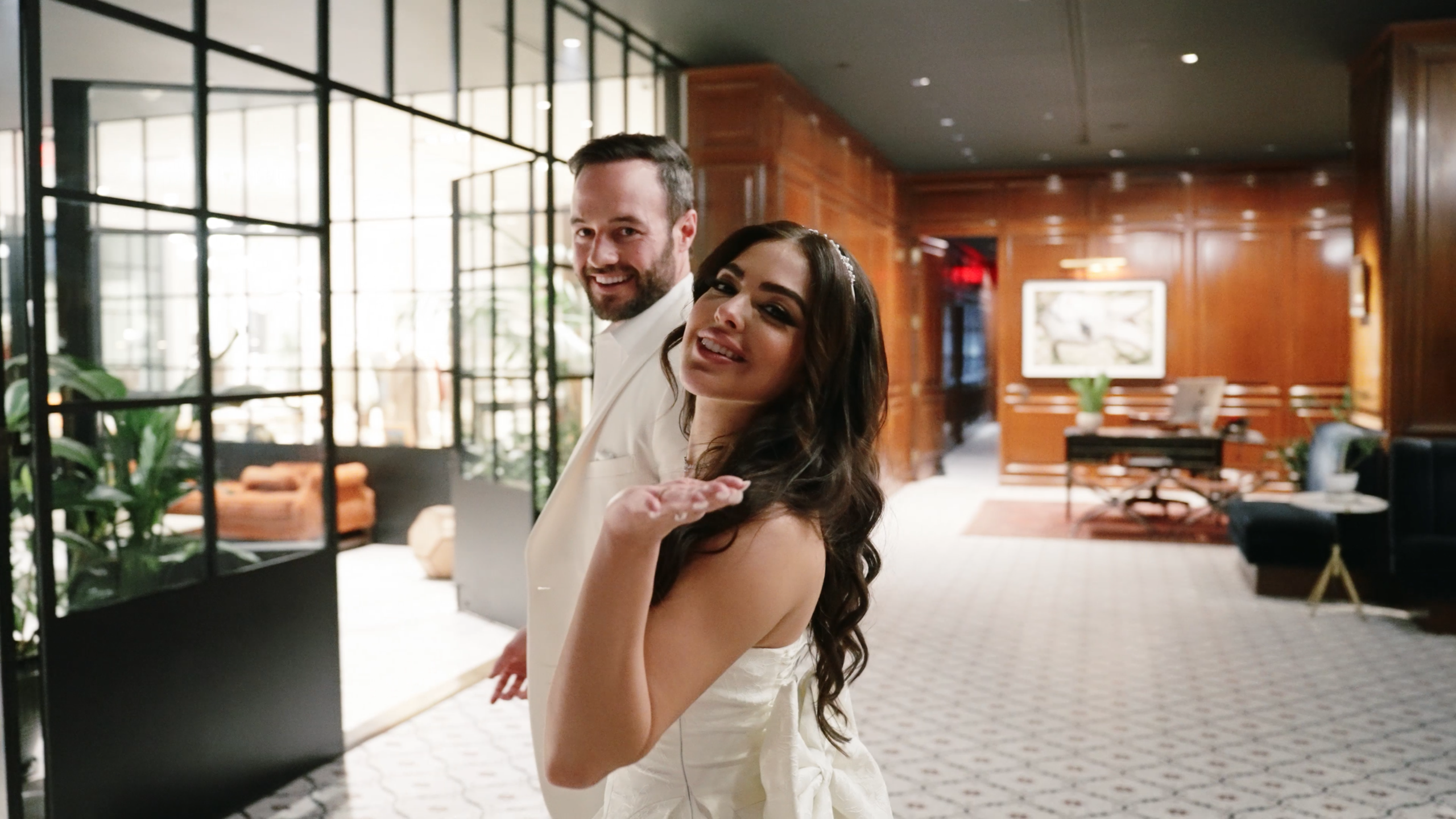 Bride blowing a kiss to the camera while holding the groom’s hand, smiling on their wedding day.