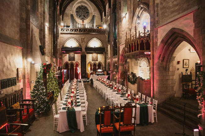 Interior wedding setup inside Hammond Castle Museum in Gloucester Massachusetts featuring historic stone walls, arched architecture, and elegant ceremony décor in a dramatic candlelit atmosphere.