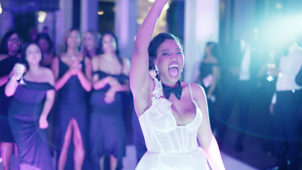 Bride laughs with excitement as she prepares to throw the bouquet behind her to her bridesmaids at her reception.