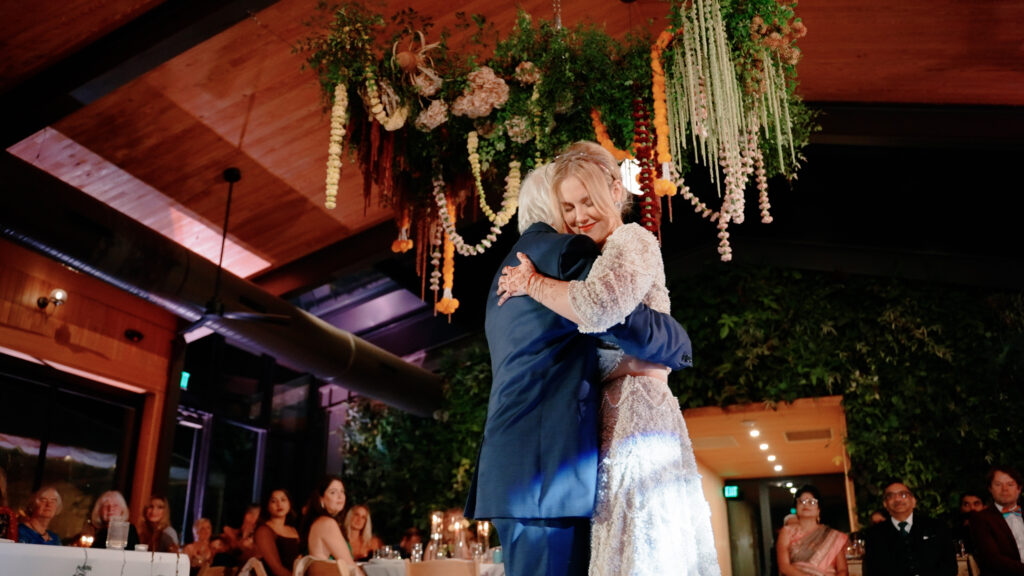 Bride and Father-of-the-Bride embrace in their dance at the reception in this interior venue with ornate flowers hanging from above.