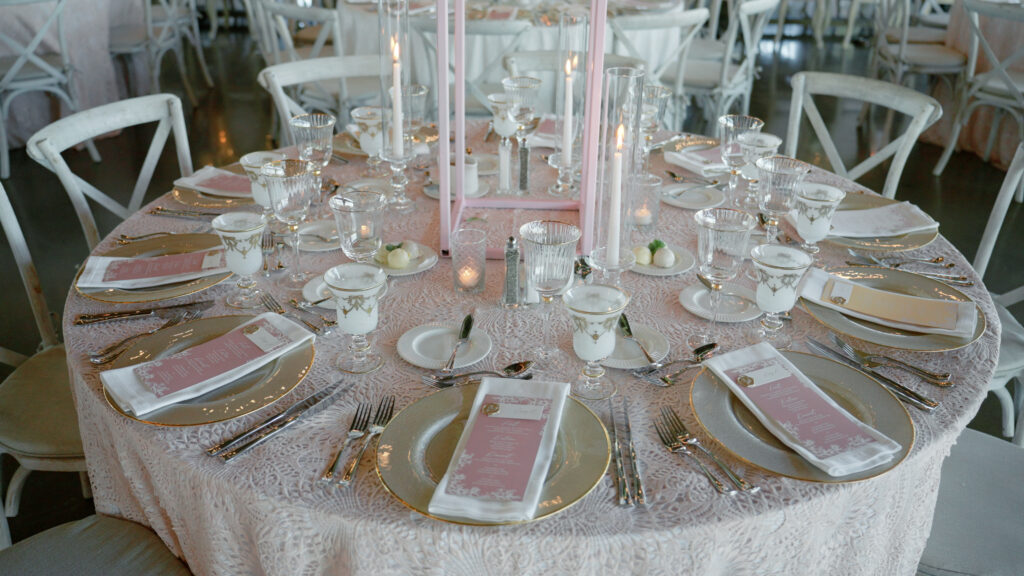 Interior wedding reception tablescape featuring elegantly arranged table settings, romantic floral accents, and glowing candlelight in a refined coastal venue setting.