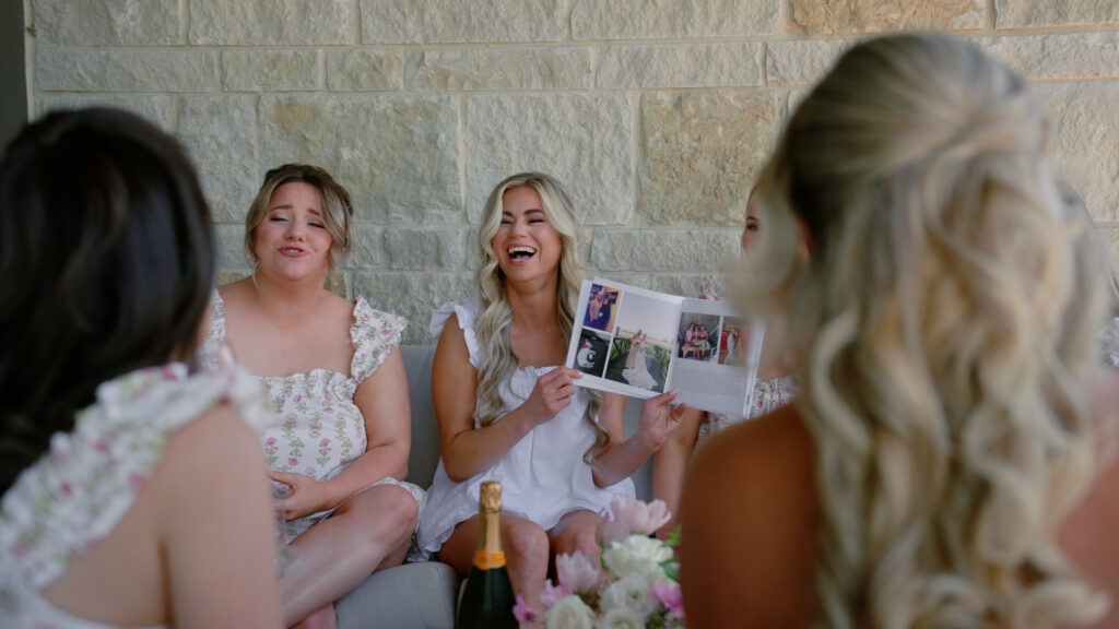 Bride laughing with bridesmaids as they look through a photo album before the wedding.