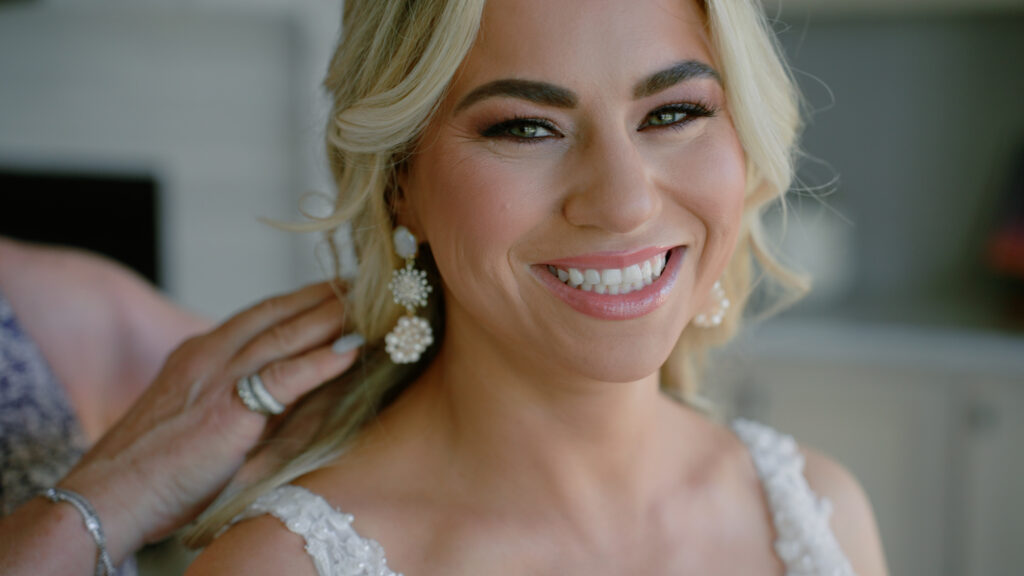 Bride smiling at the camera as her mother touches her hair.