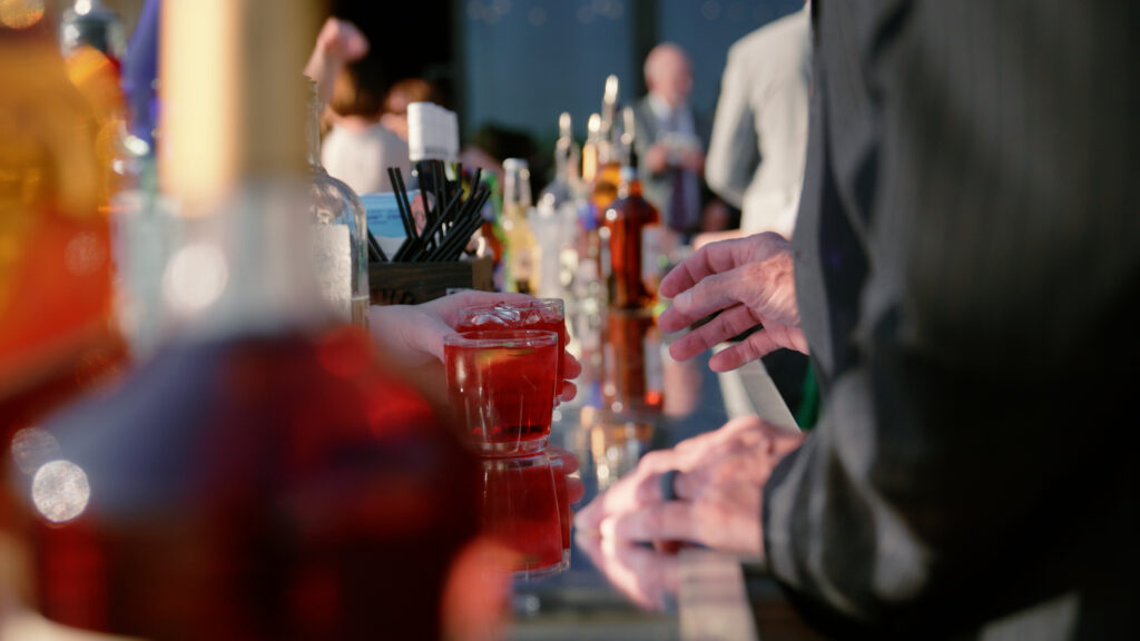 A tight shot of a bar at a wedding in Dallas, Texas, as a bartender hands a guest a red cocktail.