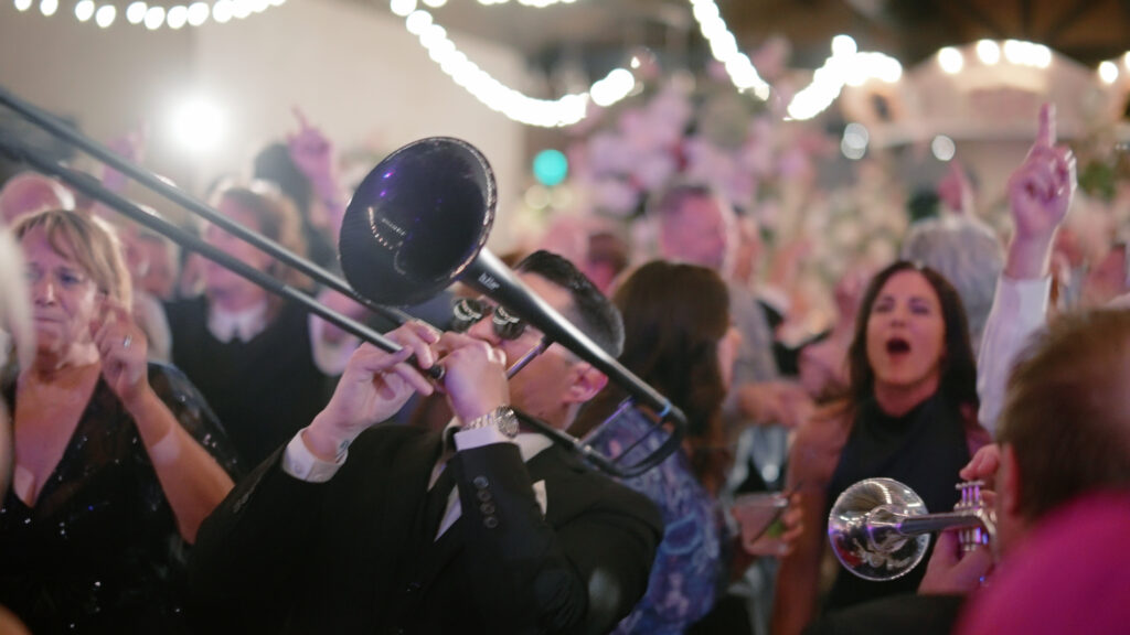 A live band plays at a wedding, with brass instruments as the focal point, and guests in the background at this Dallas venue.