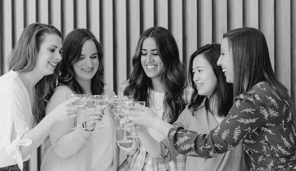 The wedding planners of Keestone Events laugh together as they toast each other in this black and white photo.