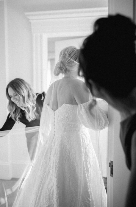 Owner of Always Yours Events in Boston, Massachusetts, fixing the dress of a bride, which reflects an elegant and detail-focused wedding planning brand.