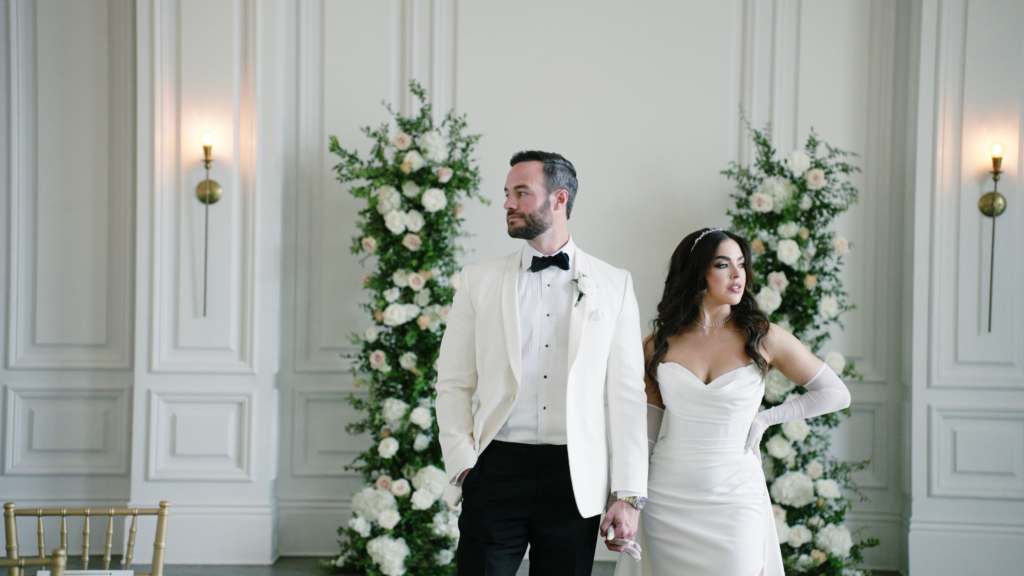 Bride and groom holding hands while standing in a wedding ceremony space, looking in opposite directions during an emotional moment.