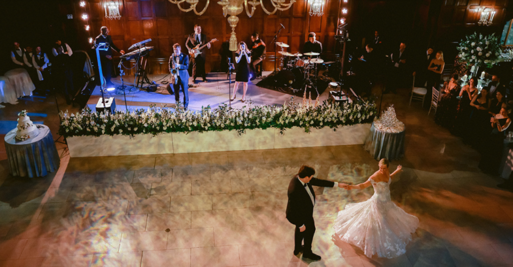 Bride and groom sharing their first dance at the Harvard Club of Boston as a live band performs and guests look on, surrounded by warm lighting and classic, elegant interiors.