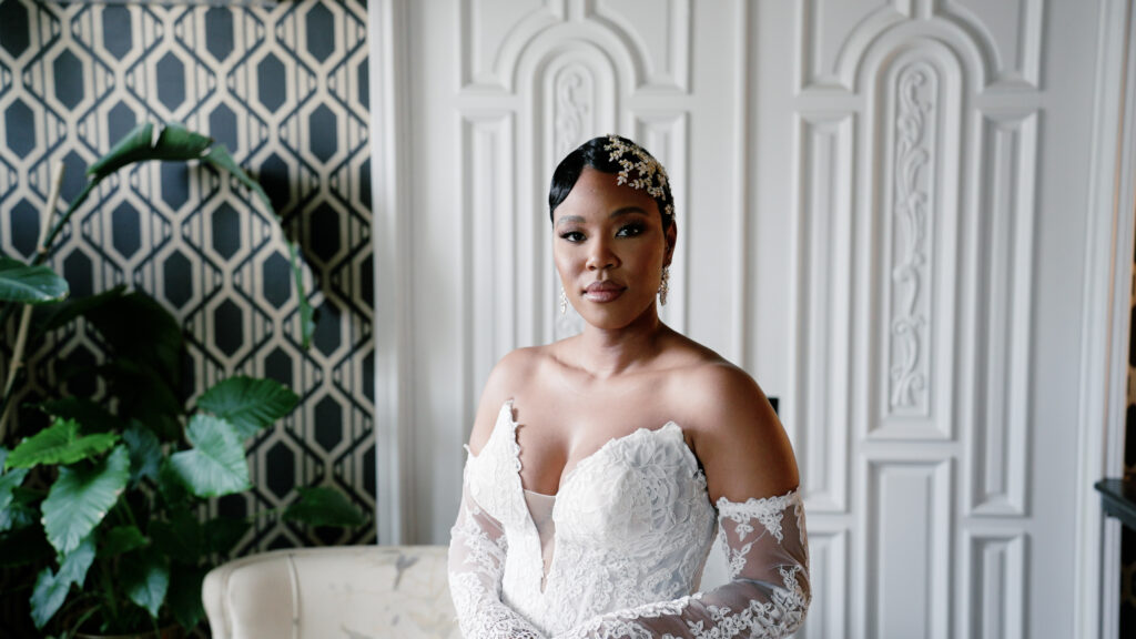 Bride smiling warmly at the camera during her wedding day, wearing elegant bridal attire and captured in a candid, joyful moment surrounded by soft, romantic lighting.