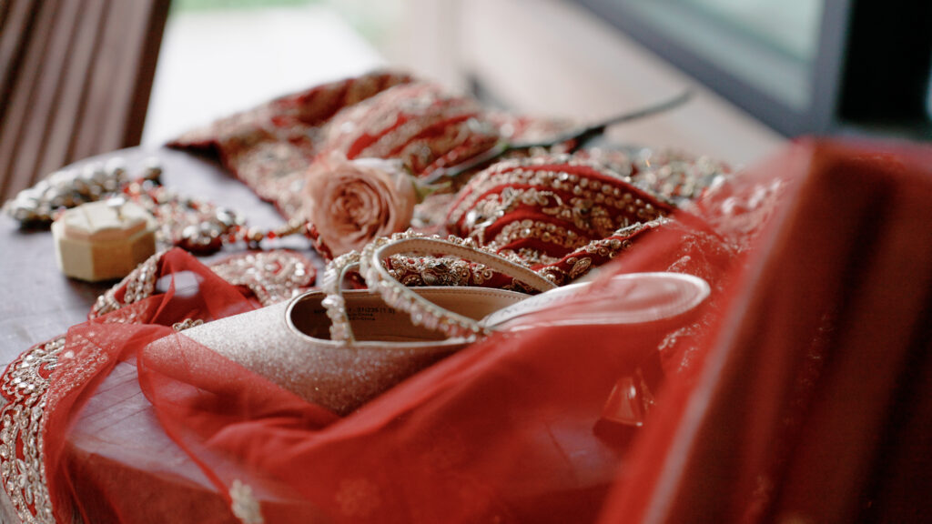 Flat lay of bridal shoes and colorful traditional garments arranged for an Indian wedding, showcasing vibrant fabrics, intricate details, and elegant wedding accessories.