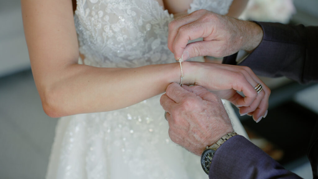 Bride’s bracelet being fastened by her father in a close-up shot, focusing on hands and jewelry without visible faces.