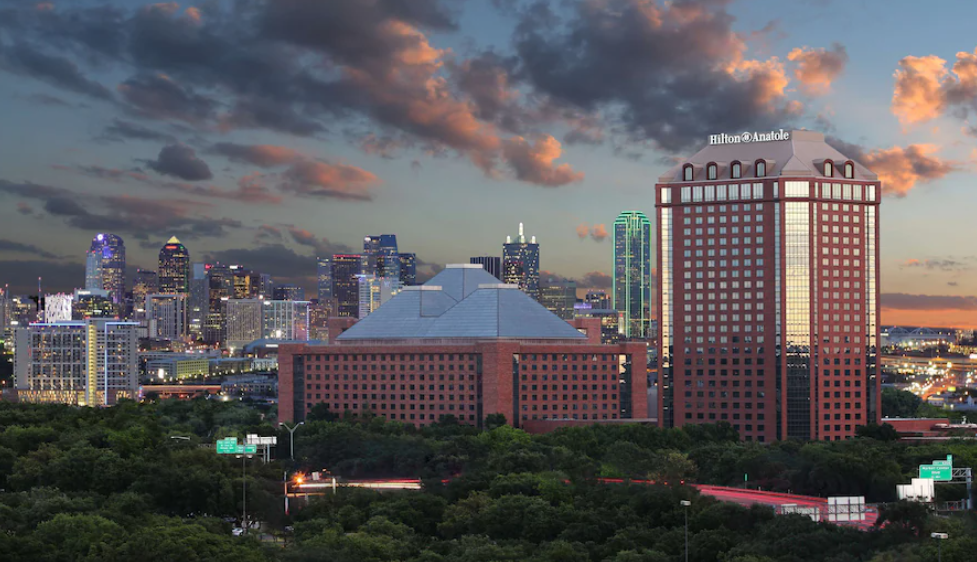 Exterior view of Hilton Anatole with surrounding Dallas buildings, showcasing the hotel’s modern architecture and city skyline backdrop.
