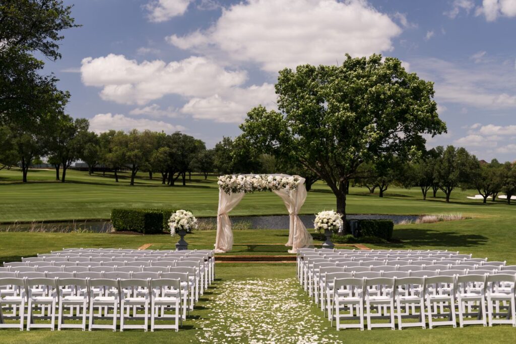 Outdoor wedding setup at The Ritz-Carlton Dallas, Las Colinas in Irving, Texas, featuring a scenic ceremony space with manicured lawns, elegant floral arrangements, and a refined resort backdrop.