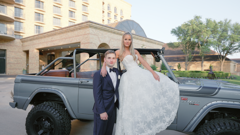 Bride and groom leaning against a car outside their wedding venue, sharing a relaxed and romantic moment together on their wedding day.