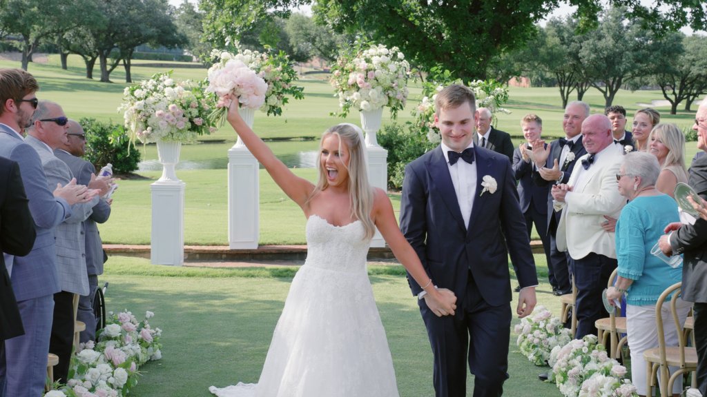 Bride and groom celebrating as they walk back down the aisle after their vows, smiling and holding hands while guests applaud during their wedding ceremony.