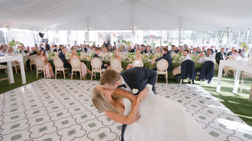 Groom dipping his bride on the dance floor under a large outdoor tent during their wedding reception, capturing a romantic and joyful celebration moment surrounded by guests and soft ambient lighting.