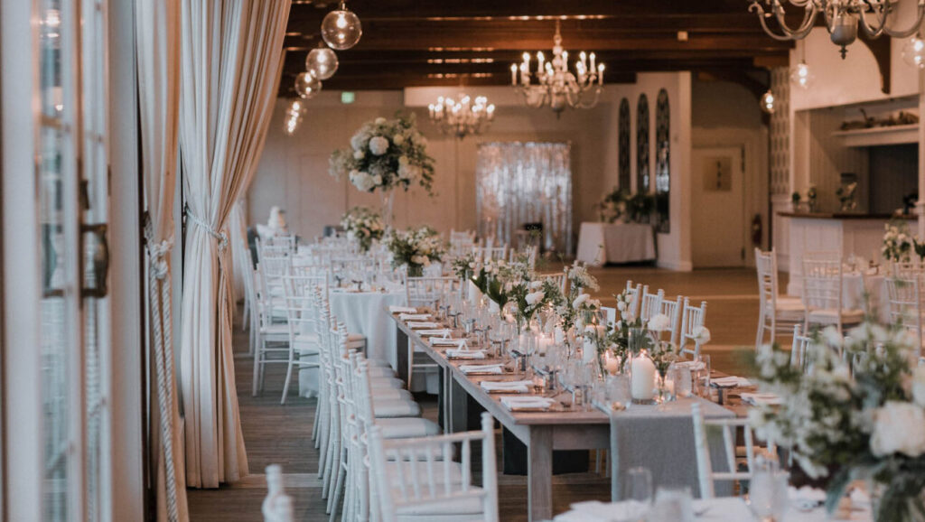 Wedding reception setup inside Wychmere Beach Club, showcasing long banquet tables with luxurious tablescapes, warm ambient lighting, and a sophisticated coastal wedding atmosphere designed for an elegant celebration.